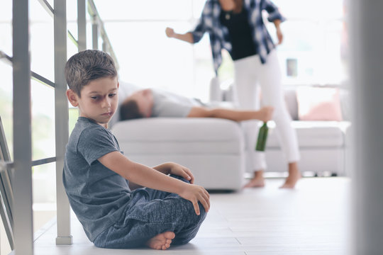 Little boy with bruise sitting on floor while his parents fighting on background. Domestic violence concept