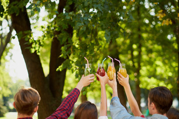 Group of people celebrate with detox juice cocktails on green nature background witn free space....