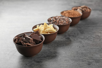 Bowls with cocoa products on grey background