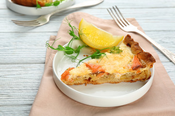 Plate with piece of salmon quiche pie on table
