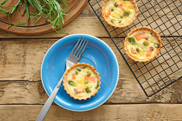 Baking grid and plate with tasty salmon tartlets on wooden table