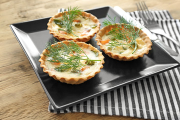 Plate with tasty salmon tartlets on table