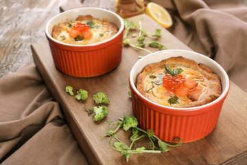Ramekins with tasty salmon tartlets on wooden board