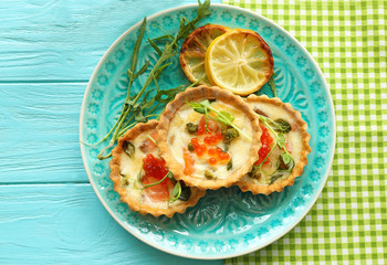 Plate with tasty salmon tartlets on table