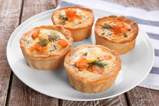 Plate with tasty salmon tartlets on table