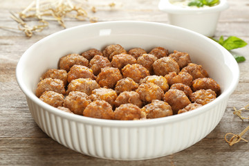 Ceramic baking dish with sausage cheese balls on wooden background