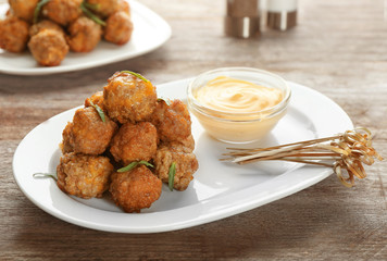 Ceramic plate with sausage cheese balls and sauce on wooden background