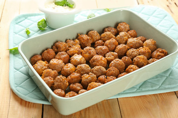 Ceramic baking dish with sausage cheese balls on wooden background