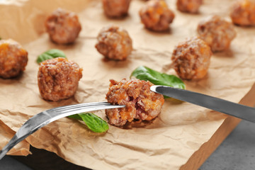 Eating of sausage cheese ball with fork and knife on wooden board