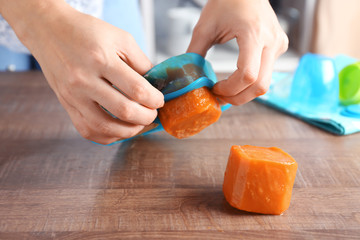Woman removing frozen vegetable puree from silicone ice tray near table