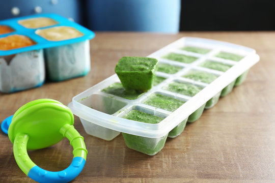 Ice tray with frozen vegetable puree on wooden table