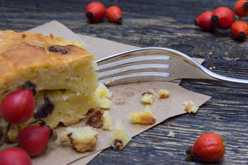 Slice pie with raisin on paper and berries rosehip and fork