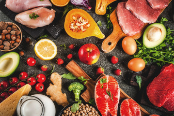Healthy diet background. Organic food ingredients, superfoods: beef and pork meat, chicken filet, salmon fish, beans, nuts, milk, eggs, fruits, vegetables. Black stone table, copy space top view