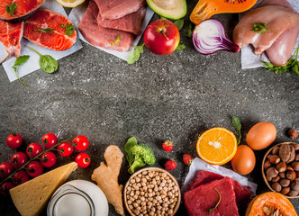 Healthy diet background. Organic food ingredients, superfoods: beef and pork meat, chicken filet, salmon fish, beans, nuts, milk, eggs, fruits, vegetables. Black stone table, copy space top view