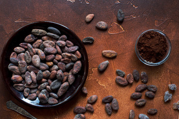 Raw cocoa beans, cacao powder and brown sugar on dark stone background