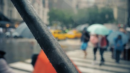 Pedestrians with umbrellas cross a rainy Manhattan street at the intersection of 6th Avenue and W 34th Street. Shot in slow motion.  	