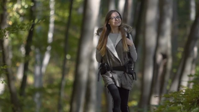 Smiling tourist girl, in glasses, walking in the forest, slowmotion on sunny fall day