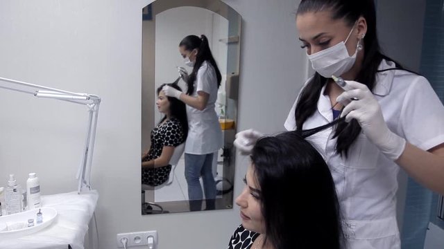In the clinic, the cosmetologist makes mesotherapy injections to the client to improve the condition of the hair