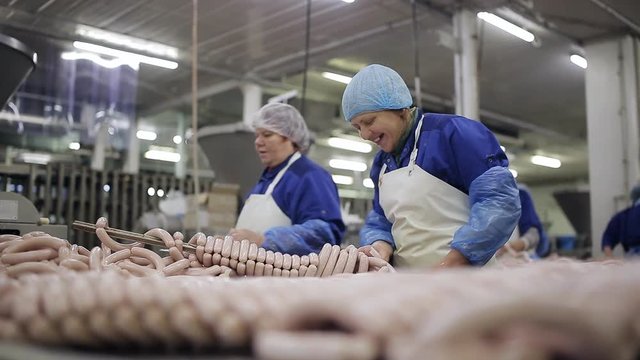 Meat Product Manufacturing. Producting Department. Employees Tying the Ends of Sausages . Worker Thread Sausages on the Metal Stick