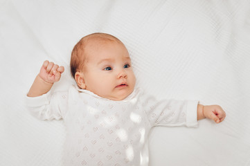 Adorable baby girl lying on white blanket and smiling, wearing heart body.