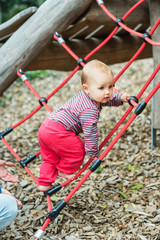 Adorable baby girl climbing the net on playground. 9-12 months old child having fun outdoors