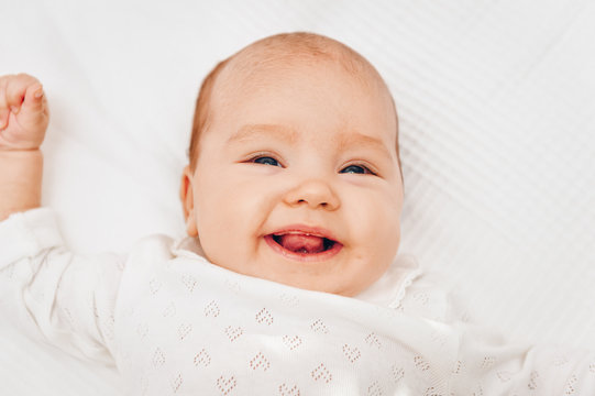 Adorable baby girl lying on white blanket and smiling, wearing heart body.