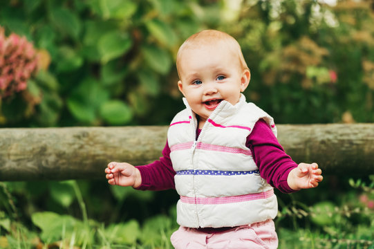 Outdoor portrait of adorable baby girl of 9-12 months old playing in the park, wearing white bodywarmer