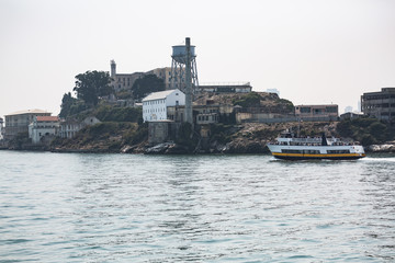 Fototapeta premium Tourist ferry boat and close up shots of Alcatraz Island in the San Francisco bay shot on a hazy summer day