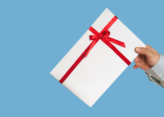 A gift in the hands of man. Close-up of a white gift box and a red ribbon. Toning and blurring. Isolated on a blue background.