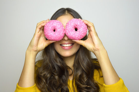 Portrait of smiling girl having fun with sweets isolated on gray background. Attractive young woman with long hair posing with doughnuts in her hands