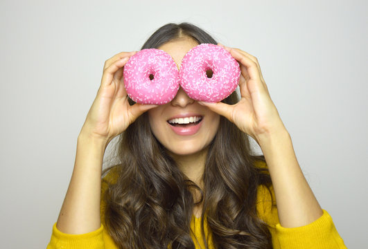 Smiling girl having fun with sweets isolated on gray background. Attractive young woman with long hair posing with doughnuts in her hands.