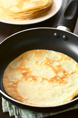 Freshly made crepe in frying pan with a stack of crepes in the back, photographed with natural light (Selective Focus, Focus in the middle of the crepe in the pan)