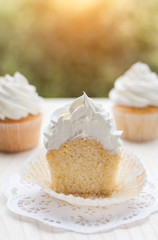 Vanilla cupcake cut in half topped with swirl of sweet vanilla frosting captured on the table in a...