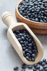 Black beans in the scoop and in wooden bowl on gray concrete background, vertical