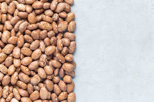 Uncooked dry pinto beans on gray concrete background, top view, copy space, horizontal