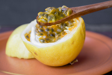 Passion fruit cut in half, ready to be eaten with wooden spoon, on brown plate, against black...