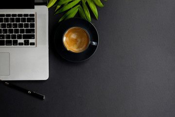 Desk workspace .desk dark workspace with black cup of coffee, laptop and plant on dark table.