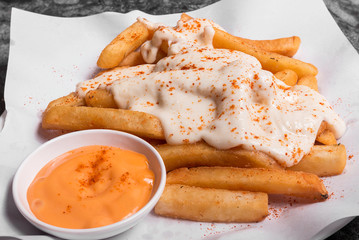 French fries on top with chesse served with sauce on plate.