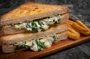 Vegetarian pressed double panini with young spinach leaves, onions and cheese served with French fries and sauce on the wooden plate.