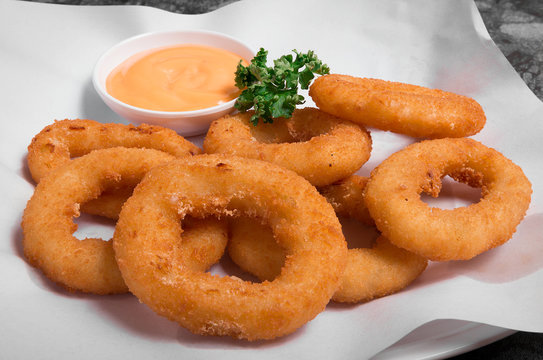 Plate of delicious looking golden onion rings or calamari ring with sauce.