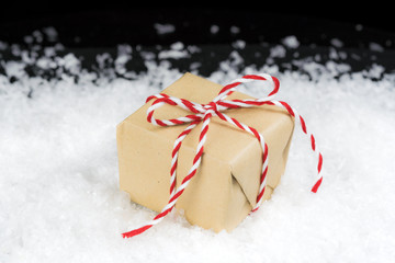 Vintage paper wrapped gift tied with red and white striped twine sitting in snow