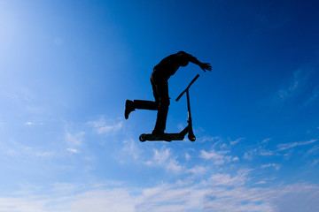 The teenager on the scooter in a jump against the background of the sky. Backlight.