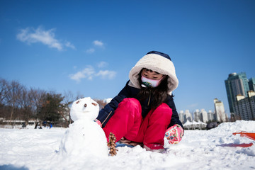 도심 공원에서 눈사람을 만들고있는 여자아이