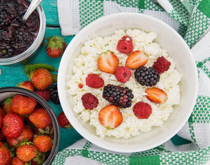 Organic cottage cheese with blackberry, strawberry and raspberry in a white ceramic bowl on the kitchen table. Dairy products for the breakfast. Healthy food concept. Top view
