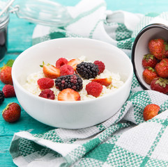 Organic cottage cheese with blackberry, strawberry and raspberry in a white ceramic bowl on the kitchen table. Dairy products for the breakfast. Healthy food concept