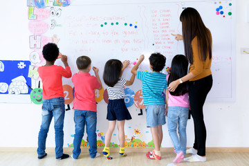 Kindergarten boys and girls  reading a book sitting on the floor learning in an international school library.
