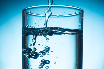 Pouring water into glass on blue background.