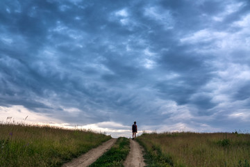 The girl is walking on the road under a cloudy sky