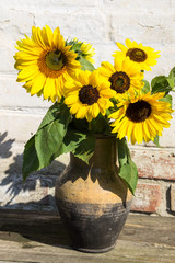 Sunflowers in vintage clay jug on wooden table
