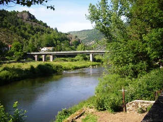 Fototapeta na wymiar Landscape of green countryside around a road bridge spanning a river. Wooded hills and sky in the background.